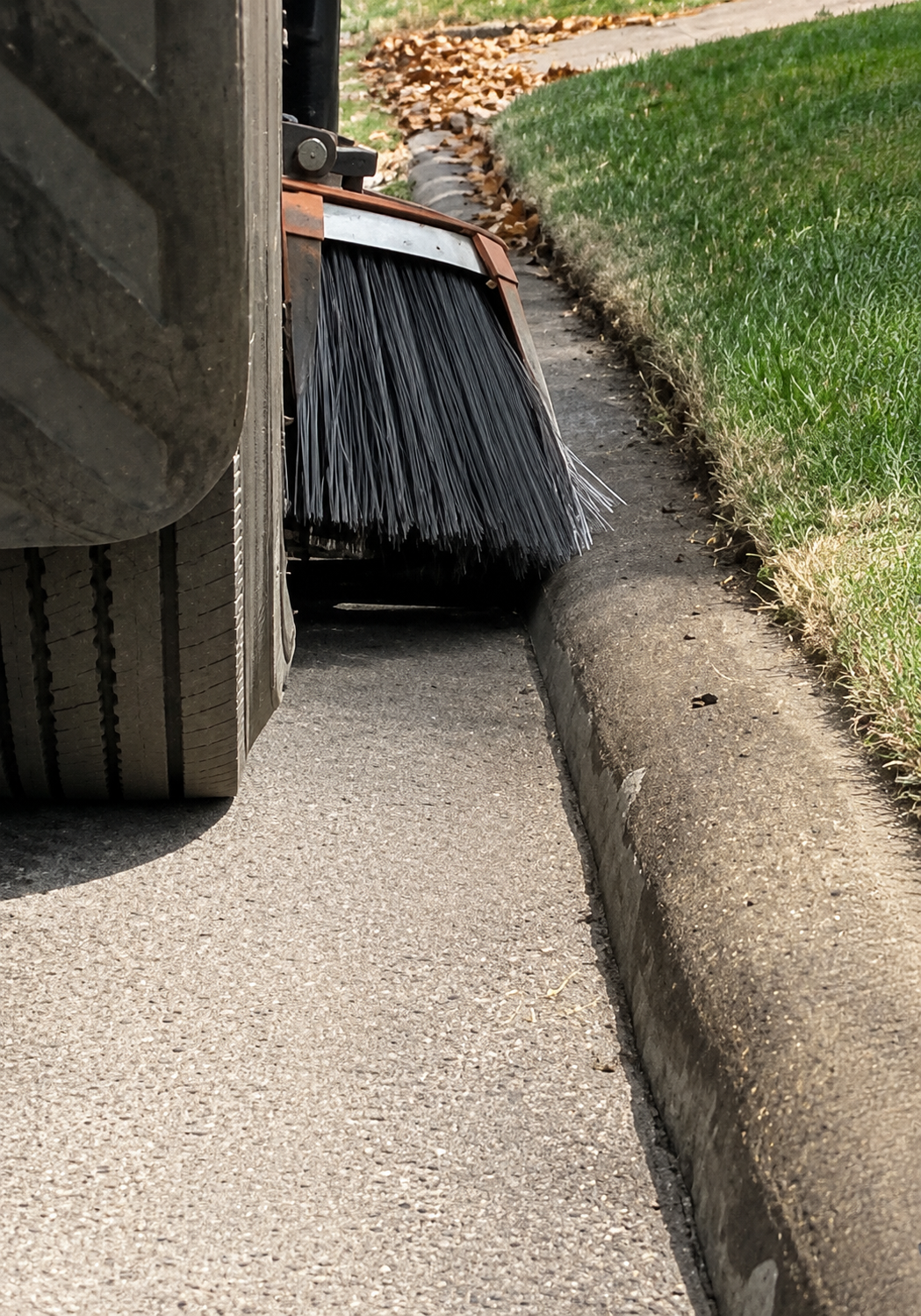 Commercial street sweeper cleaning debris along a residential community curb